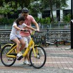Father teaches daughter to ride a yellow bicycle in a Singapore park. Bonding moment.