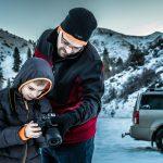 Father teaching son photography in a snowy mountain landscape.
