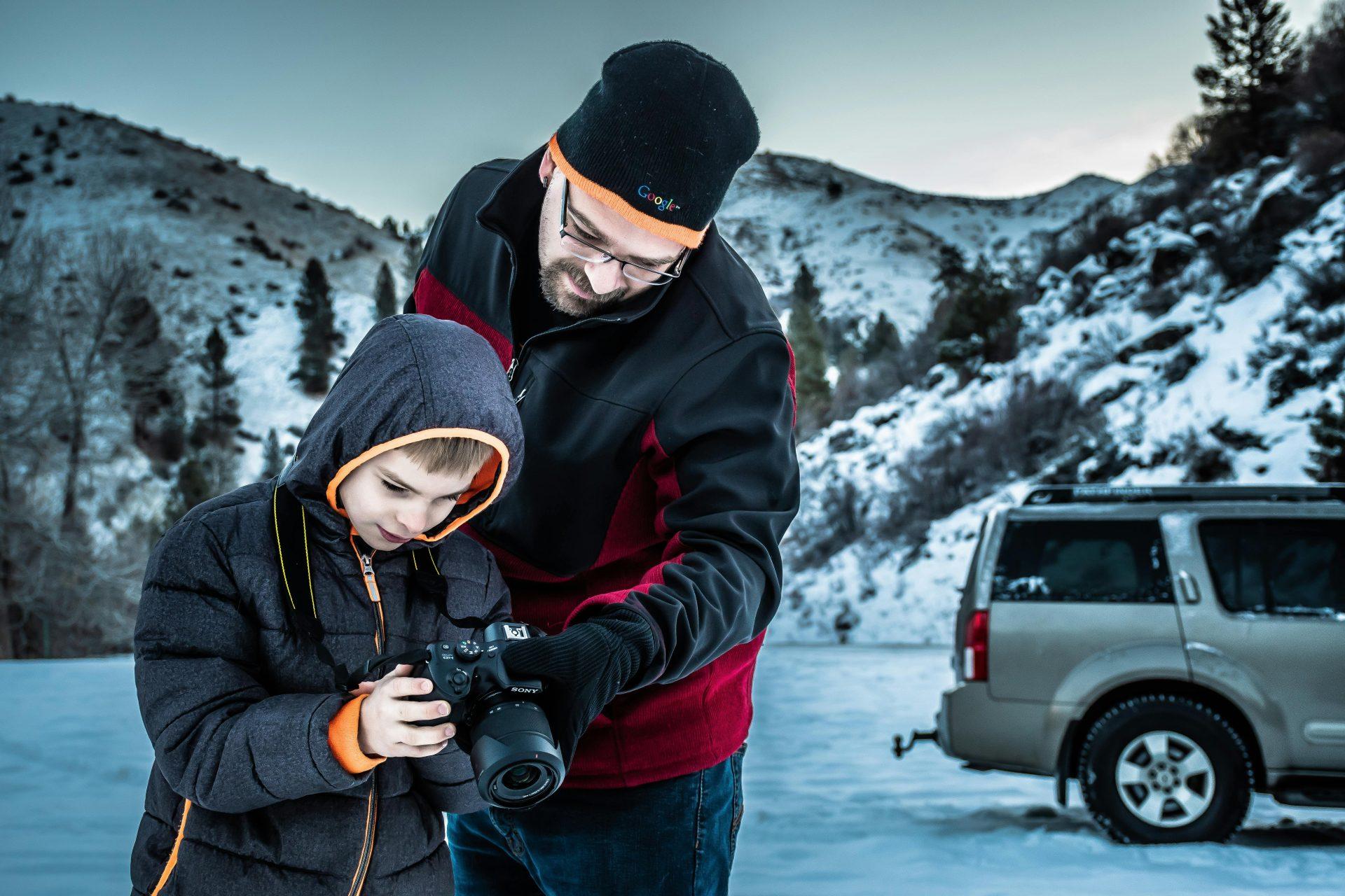 Father teaching son photography in a snowy mountain landscape.