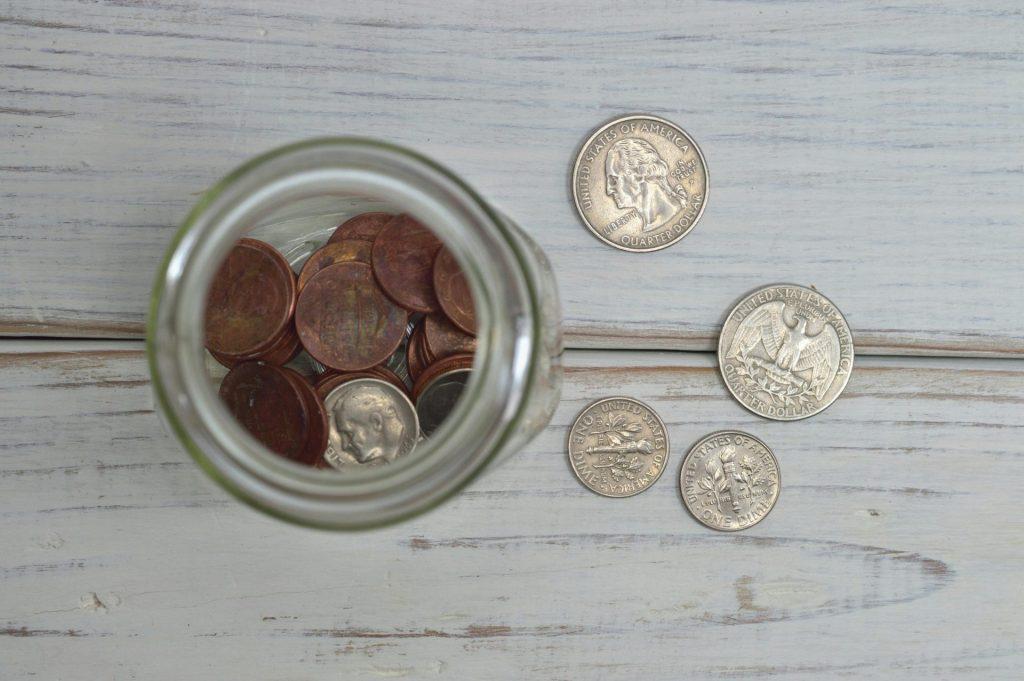 Top view of a jar filled with coins placed on a wooden table, depicting savings.